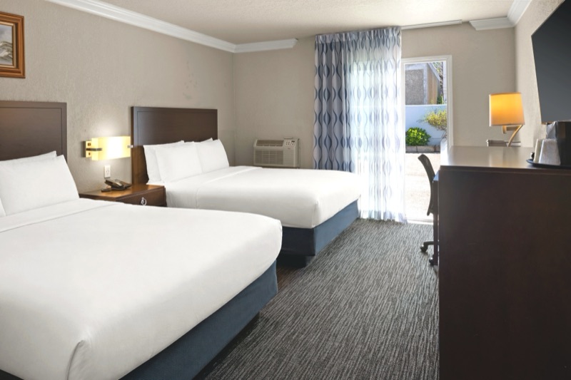 Two queen beds with a lit sconce and patio slider