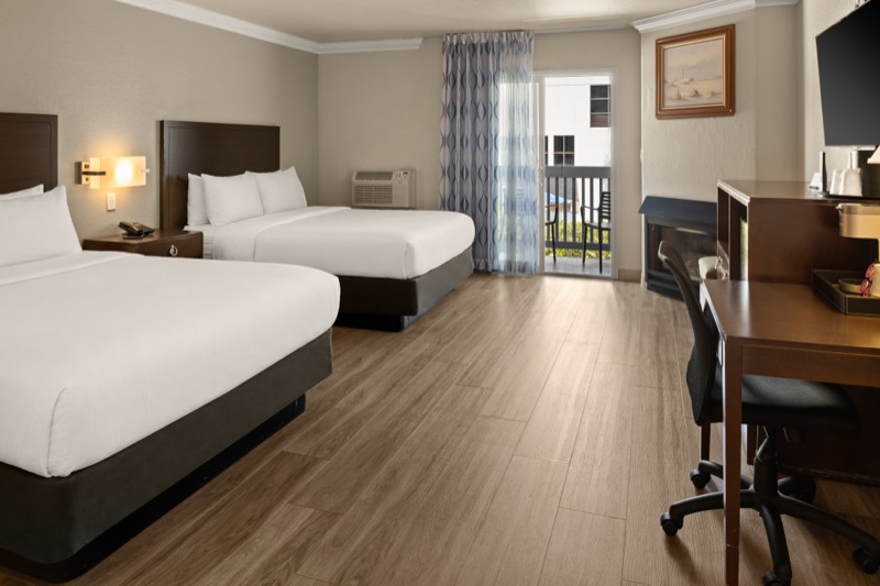 Two queen beds with lit wall sconces and a patio door to the balcony